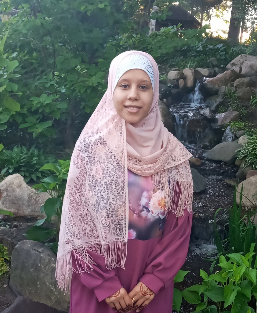 Woman in a white hijab and pink dress smiling