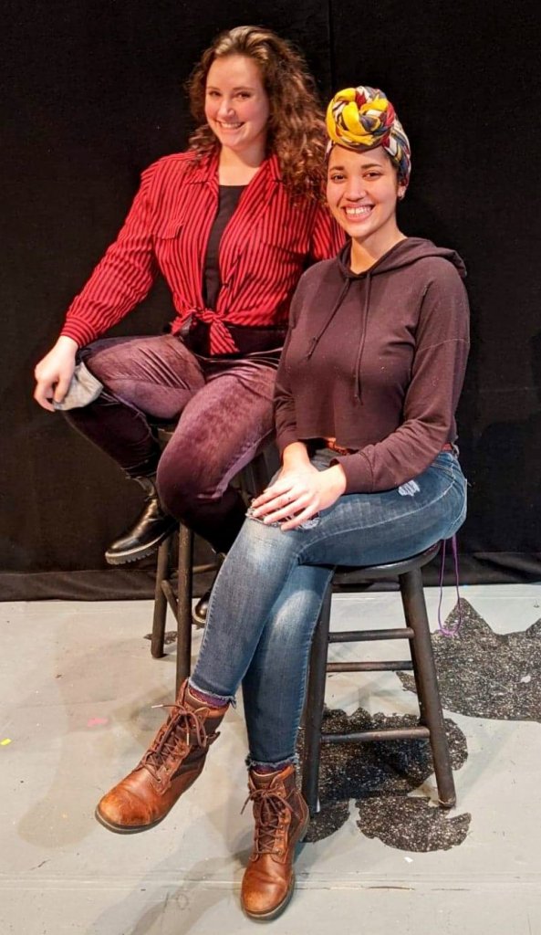 Two actors sitting in on barstools smiling at the camera