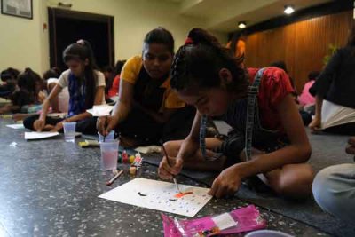 Children painting with watercolor paint on a black tile and gray carpet floor.