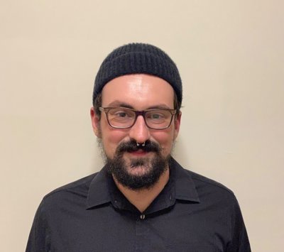 Man in black shirt, black winter hat, glasses, smiling