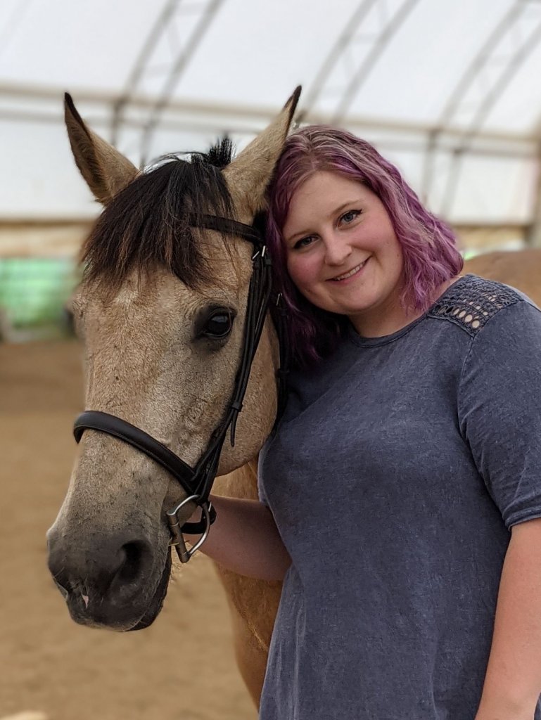 Woman in a dark blue shirt smiling, next to a horse.