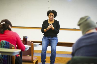 Professor sitting on a desk speaking to students