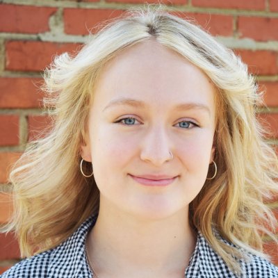 Woman in black and white checkered shirt smiling in front of a brick wall