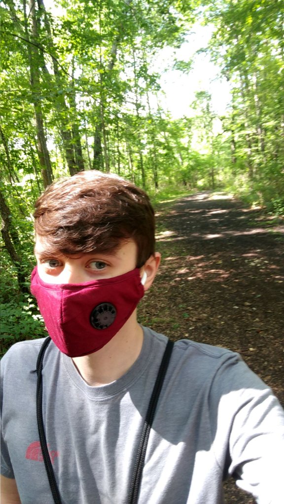 Man wearing a red face mask standing on a path in the woods