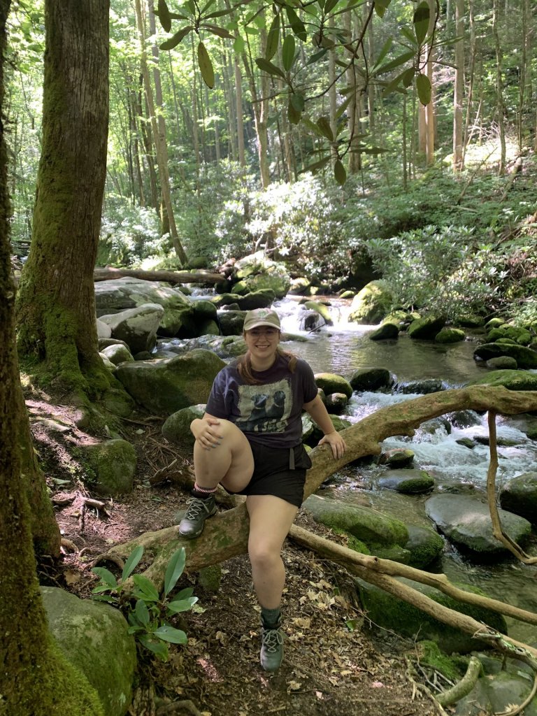 Person sitting on log by running water in the woods