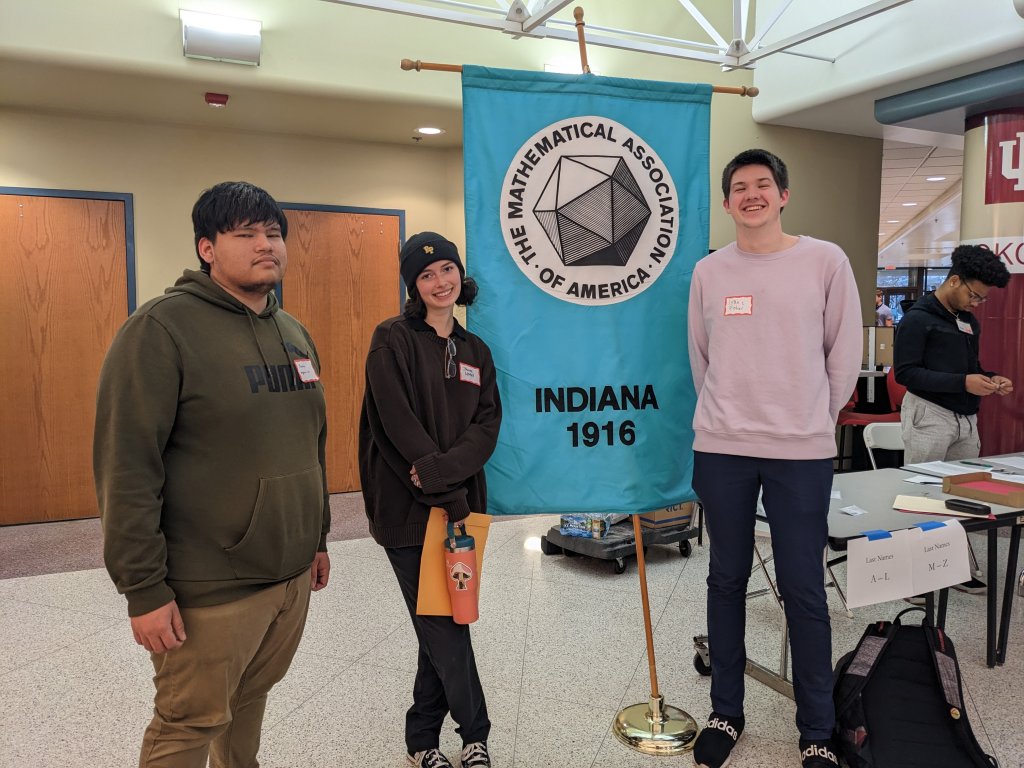 Marlon Aparacio, Johanna Morford-Obertz, and Isaac Fisher pose around the Mathematical Association of America banner after the competition.