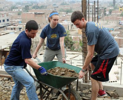 Brian, Leah and Joel lift a rock-laden wheel barrow.