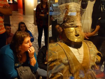 The students admire a mummy, in a sitting fetal position, with a gold mask.