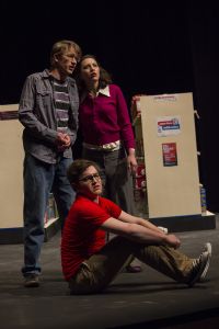 During a routine trip to the drugstore, characters played by Karsten Hess and Adrienne Schmucker (standing) and Brett Conrad (sitting) get more than they bargained for. "Stay Tuned" points a snarky finger at the media and marketing that constantly vie for our attention, and how these voices manifest in our daily lives.