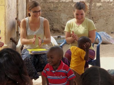 Lydia Alderfer (left), a 2013 graduate with a degree in sociology, and Maddie Ruth (right), a 2014 graduate with a degree in music and psychology, provide a beat for young dancers in Ndombo Mbodjienne, a small town in northern Senegal. The two served at an organization run by local women that processed dairy products during Study-Service Term in 2012. (Photo provided)