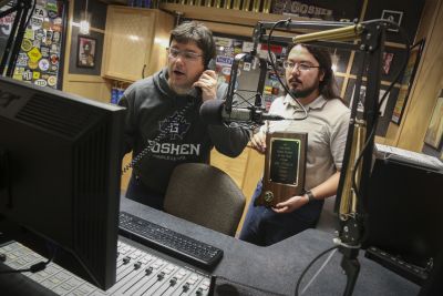 Jason Samuel, WGCS General Manager, takes a call in station. Student Station Manager Victor Garcia holds the 2016 Indiana Radio School of the Year award. 