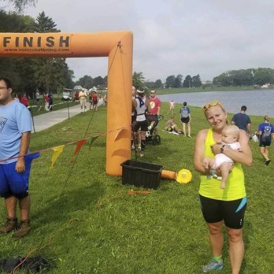 A woman holding a baby at a finish line by a body of water