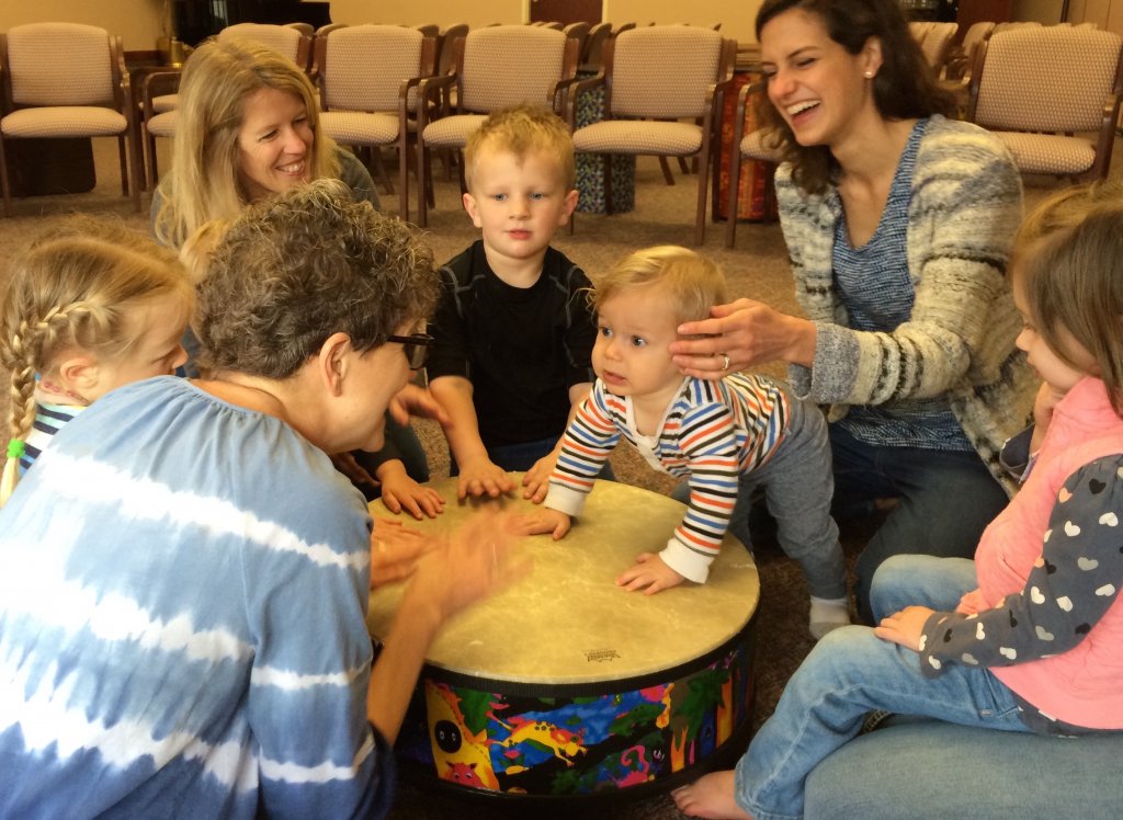 Moms and toddlers paling on a large drum in the middle of their circle.