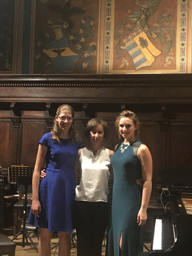 Two female students stand with their violin teacher
