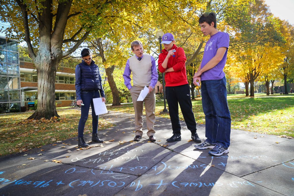 Four male students work with Professor David Houseman on equations outside on the sidewalk using chalk.