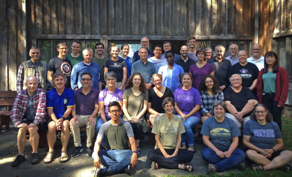 Many professors, staff, and students posing for a picture outside, sitting on benches and the sidewalk.