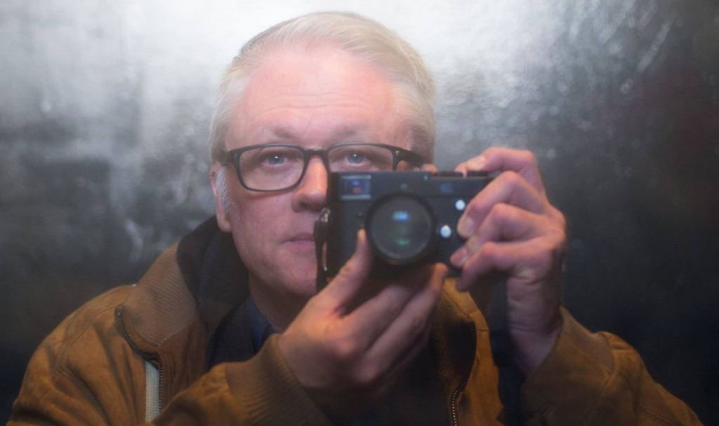 Man Taking a picture of himself in the mirror with a hand held camera.