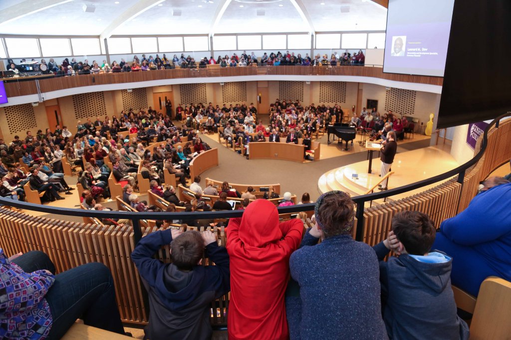 A chapel full of people listening to a person speak on stage