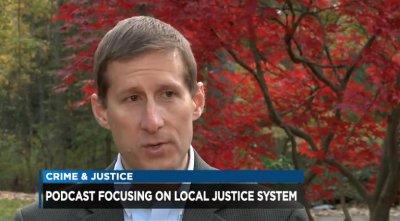 Man speaking in front of a tree. The bottom of the picture says 'Crime & Justice Podcast Focusing On Local Justice System'