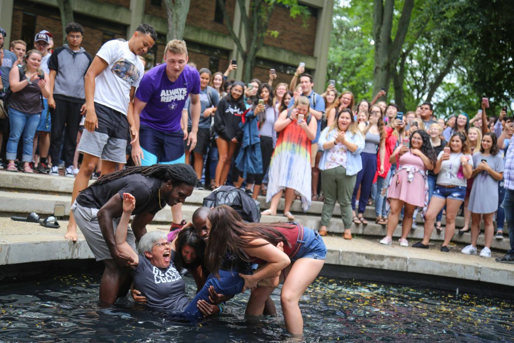 Four students dunk President Becky in the fountain surrounded by the student body