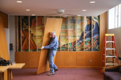 A man taking apart a wall to see a beautiful, multicolored mural that had been hidden for years.