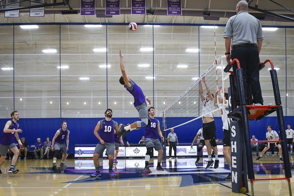 Man from Goshen's volleyball team reaching for the volleyball in the air, ready to spike it across the net.