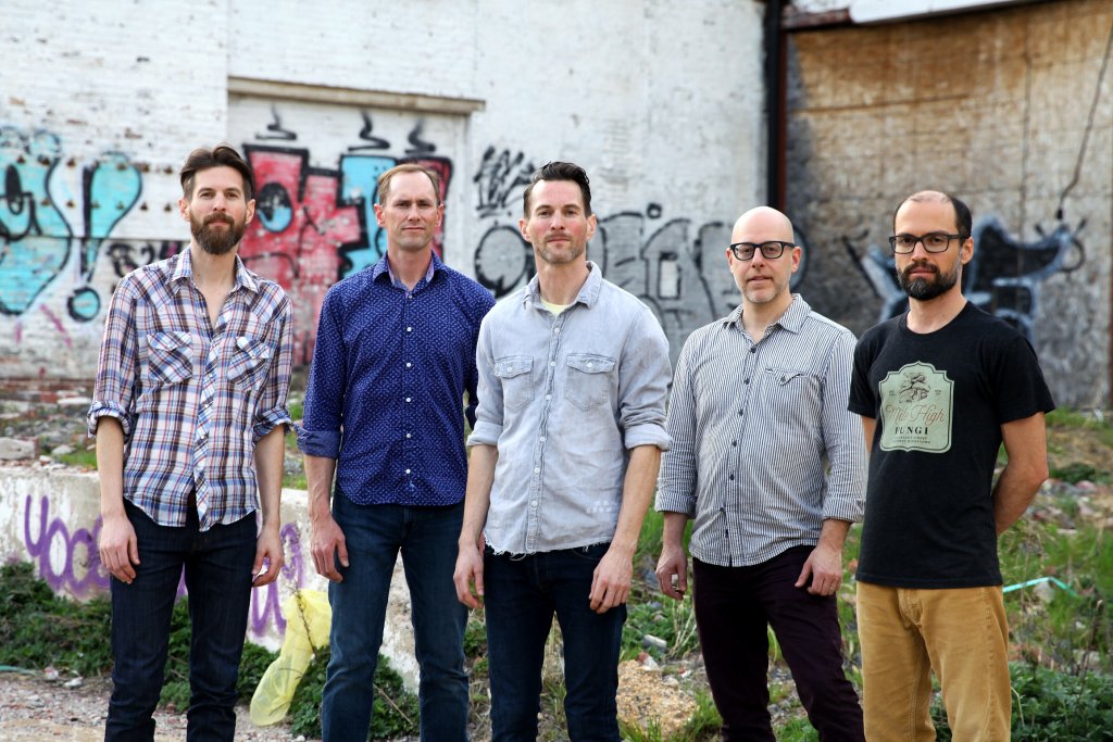 Five males standing in front of buildings with graffiti on the walls