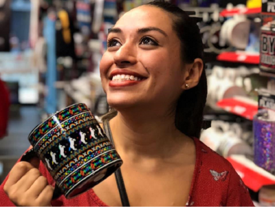 Jessica Davila smiling and holding a colorful unicorn mug in a store.