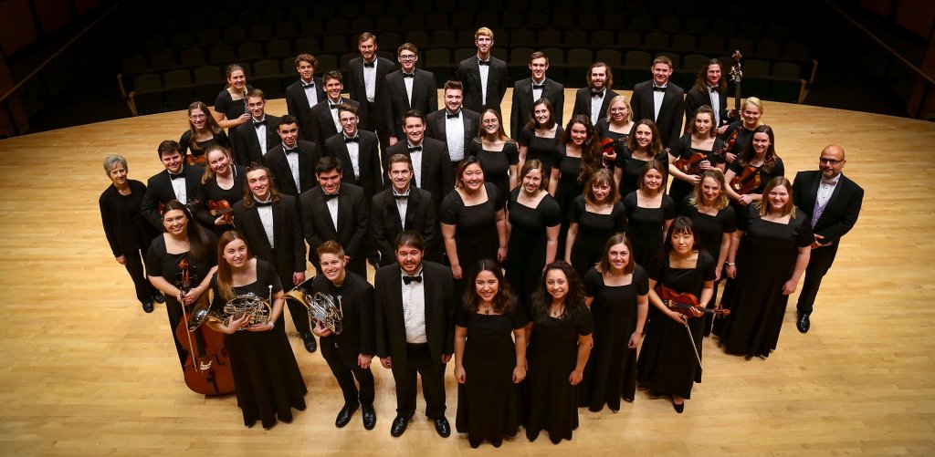 Men and Women looking up for a picture in their performance attire, while some hold their instruments.