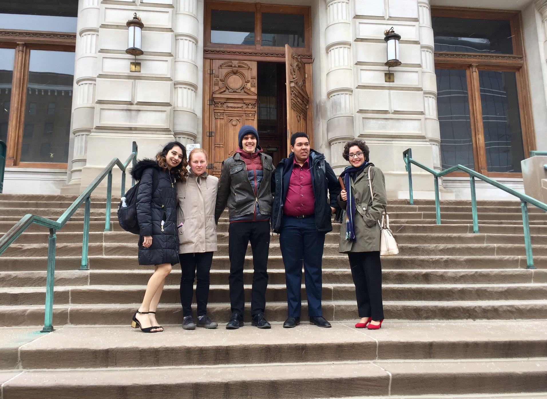 Three female students and two male students on steps in front of a door.