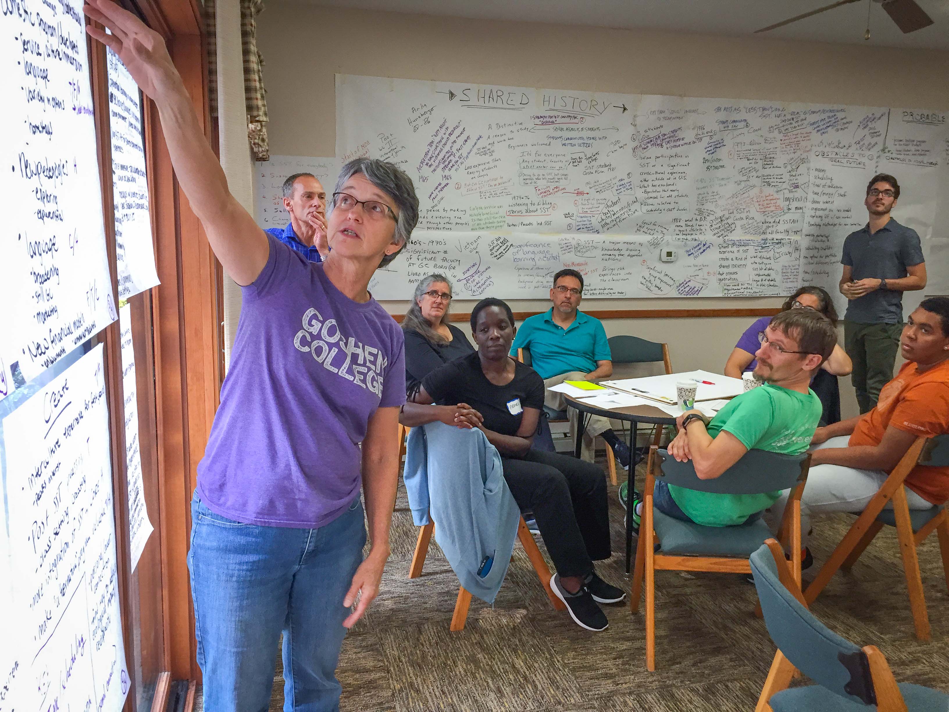 Woman pointing at papers on the wall as eight people look on.