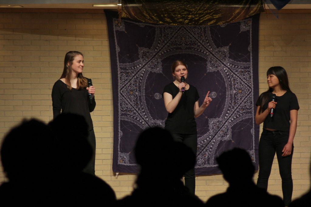 Three women dressed in black on stage with a patterned cloth behind them