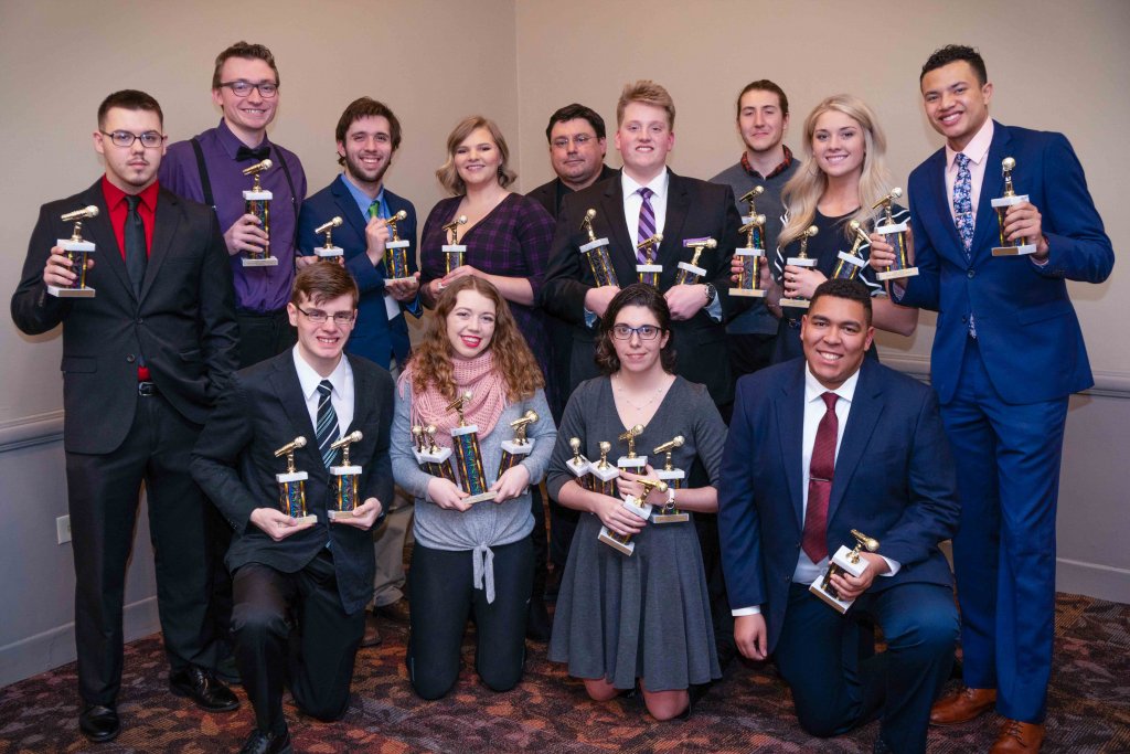 Several students dressed up holding trophies with microphones on them