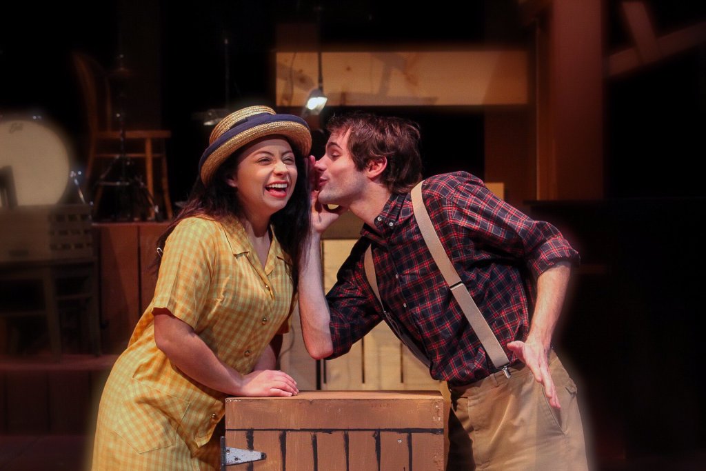 Two students playing character roles in a musical. Male is telling the female a secret while the female is laughing