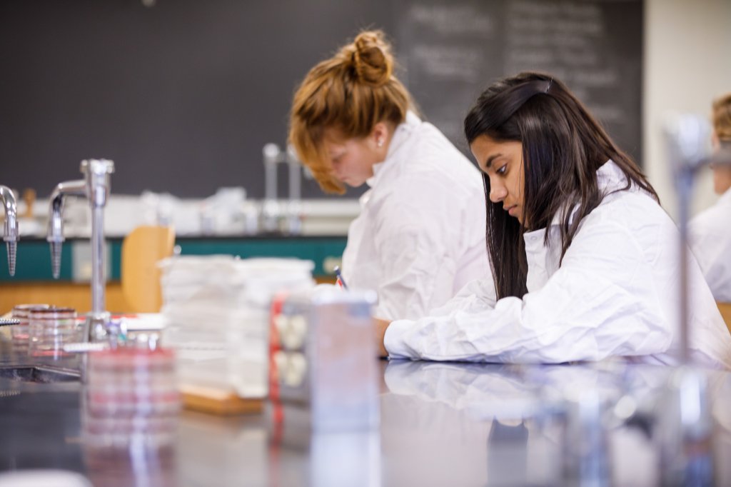 Two students wearing white lab coats working in a lab