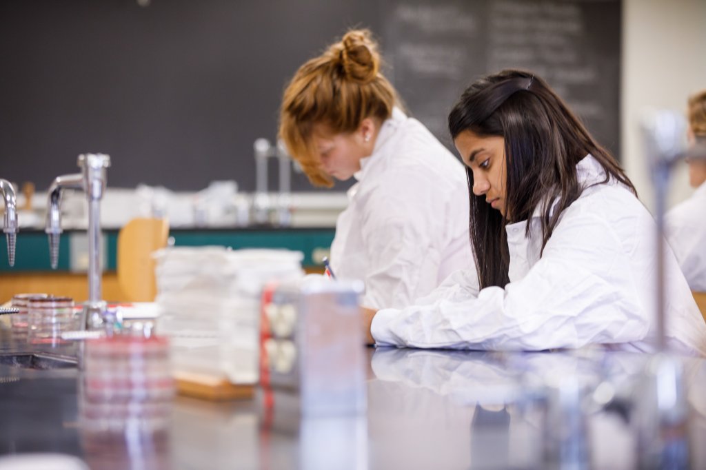 Two students wearing white lab coats working in a lab