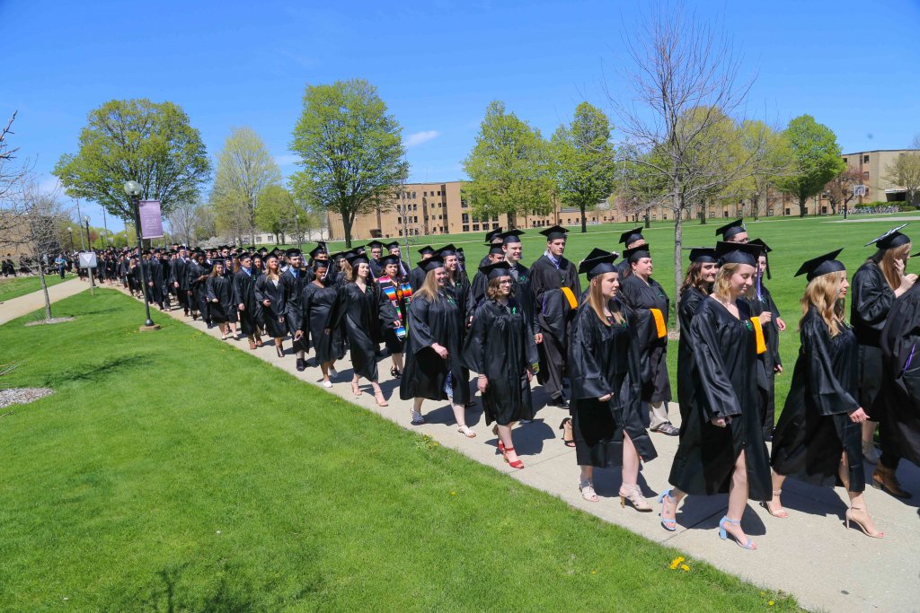 Students wearing caps and gowns walking down the sidewalk