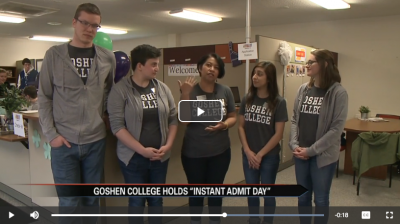 A picture of a video. A man and four women in a row wearing grey Goshen College shirts