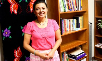 Rocio Diaz standing in front sewn flower wall hanging and next to bookshelves