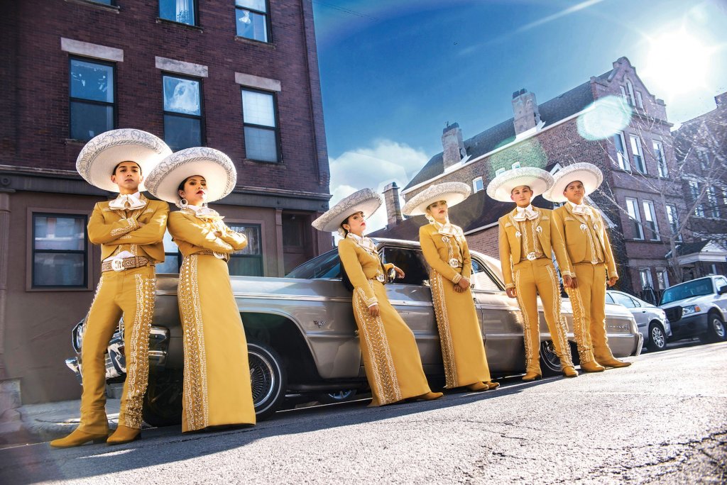 Six people in traditional Mexican attire leaning against a silver car