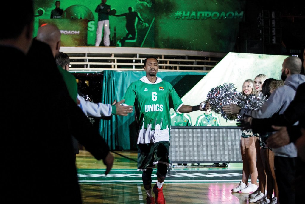 Man in a green and white basketball jersey high-fiving people