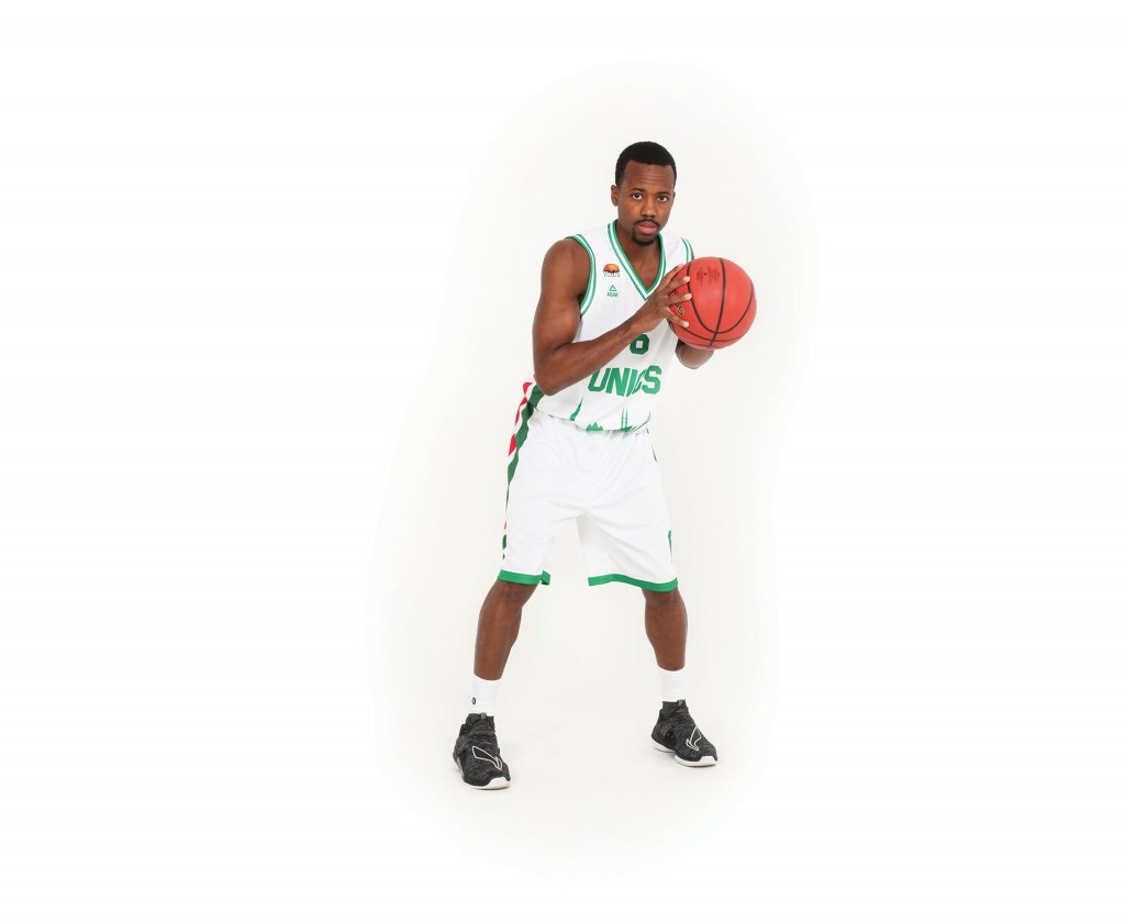 Man in a white jersey with green borders on it holding a basketball