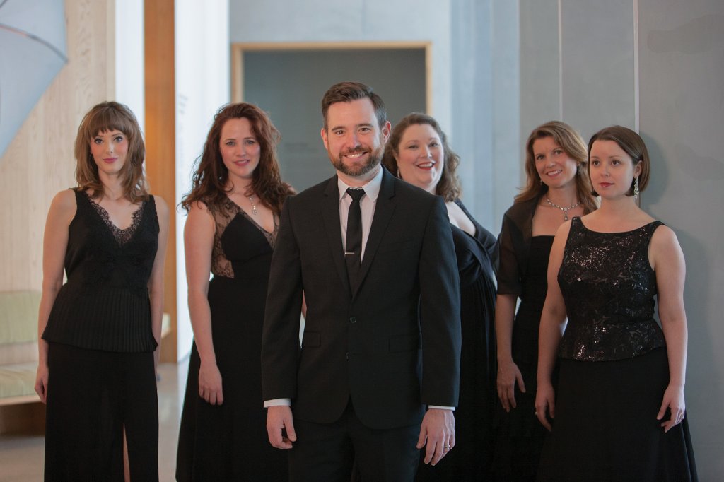 Five women wearing black standing behind a man in a black suit