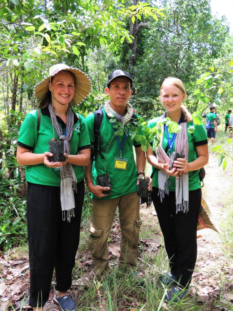 Three People wearing green shirts. Two women with a man in the middle. Each are holding a pot.