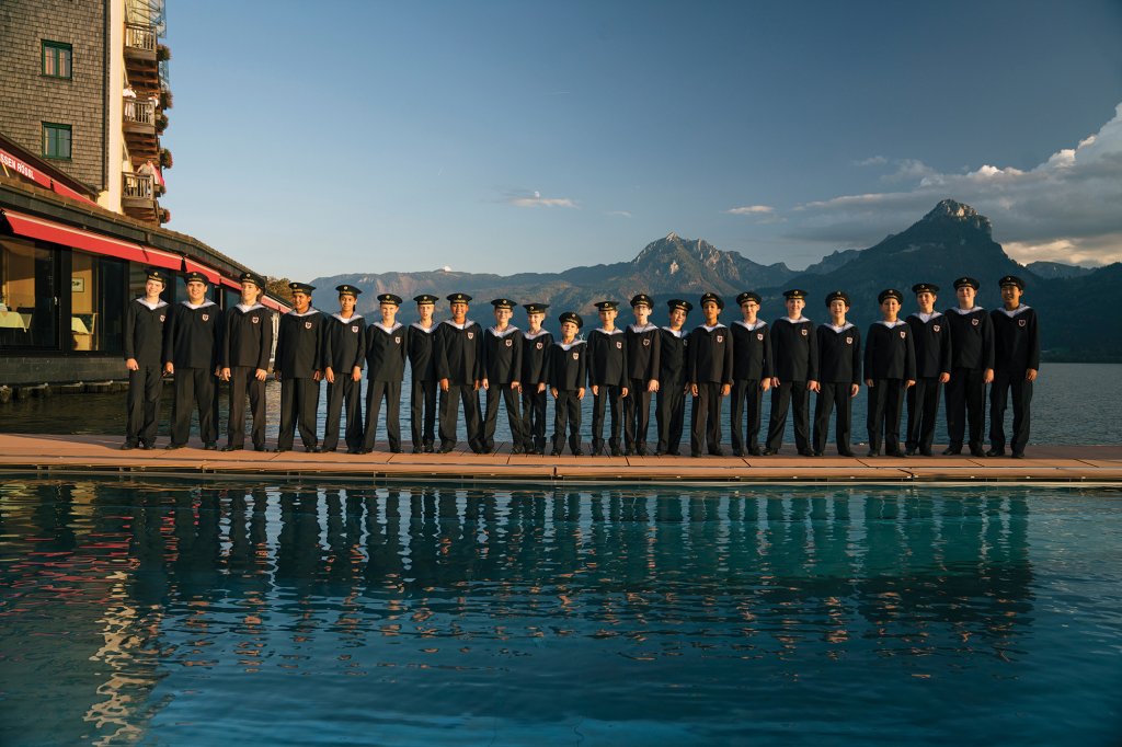 Group of boys in sailors uniforms standing on a beach between bodies of water