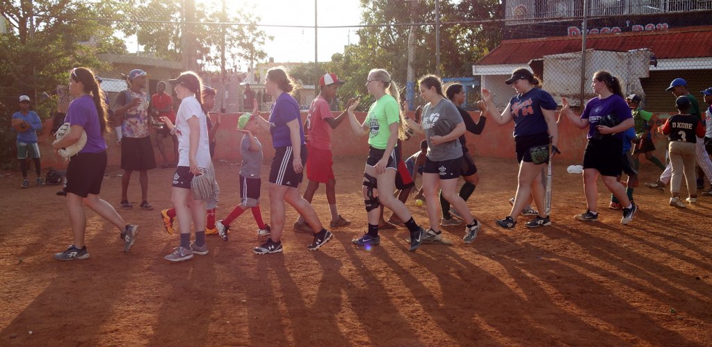 A group of people walking across a softball field