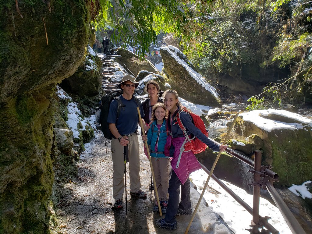 Four people; two adults and two children stand next to running water and mossy rocks