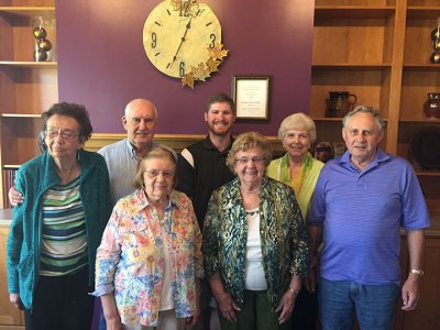 Seven people standing in front of a purple wall with a clock. Four women and three men.