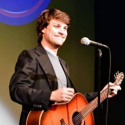 Man standing in front of a microphone holding a guitar