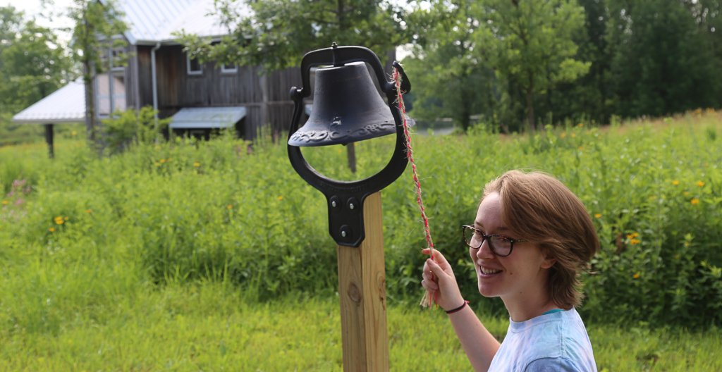 Woman ringing a bell in front of a field